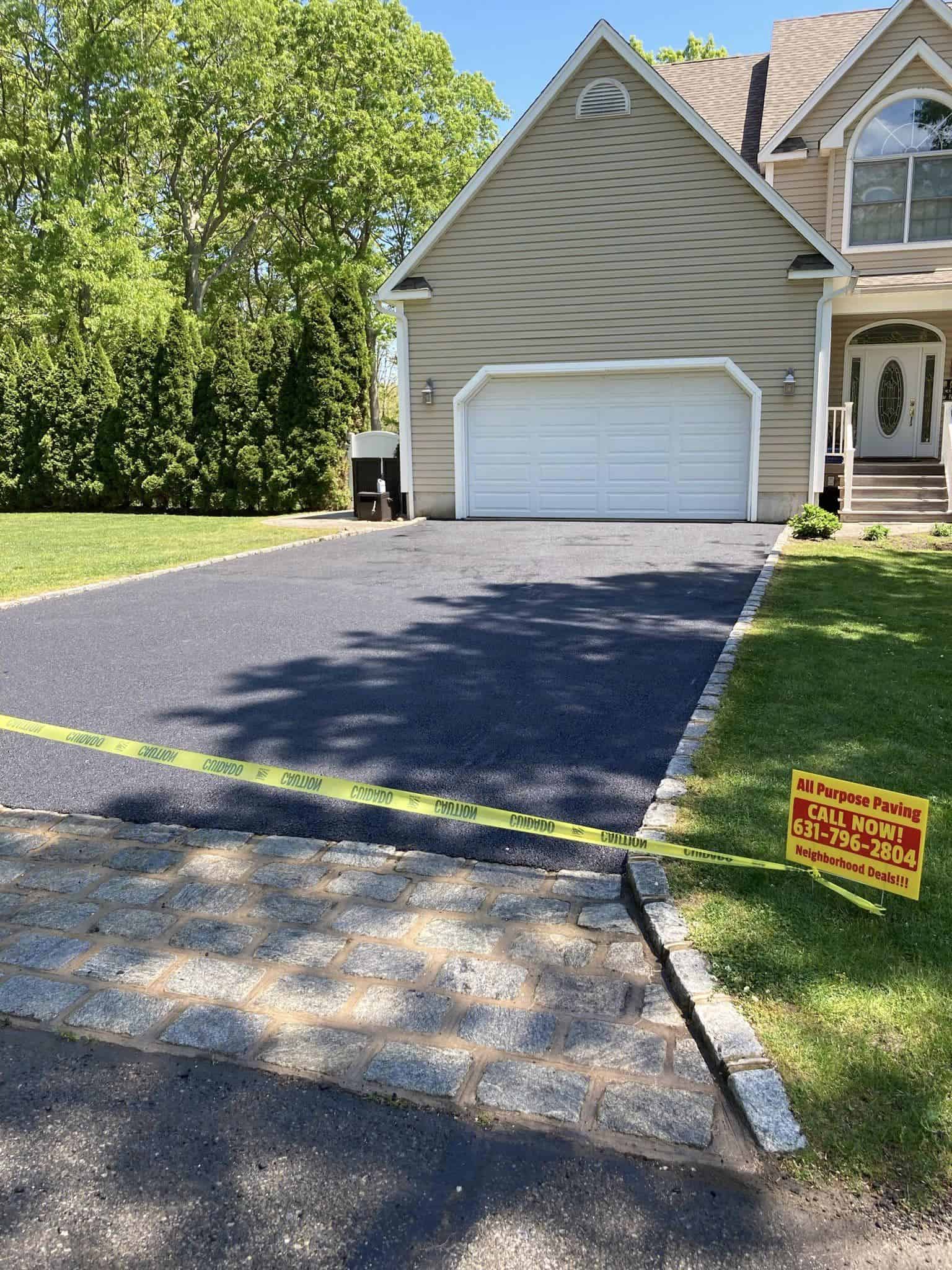A paved driveway blocked with caution tape in front of a tan colored home.